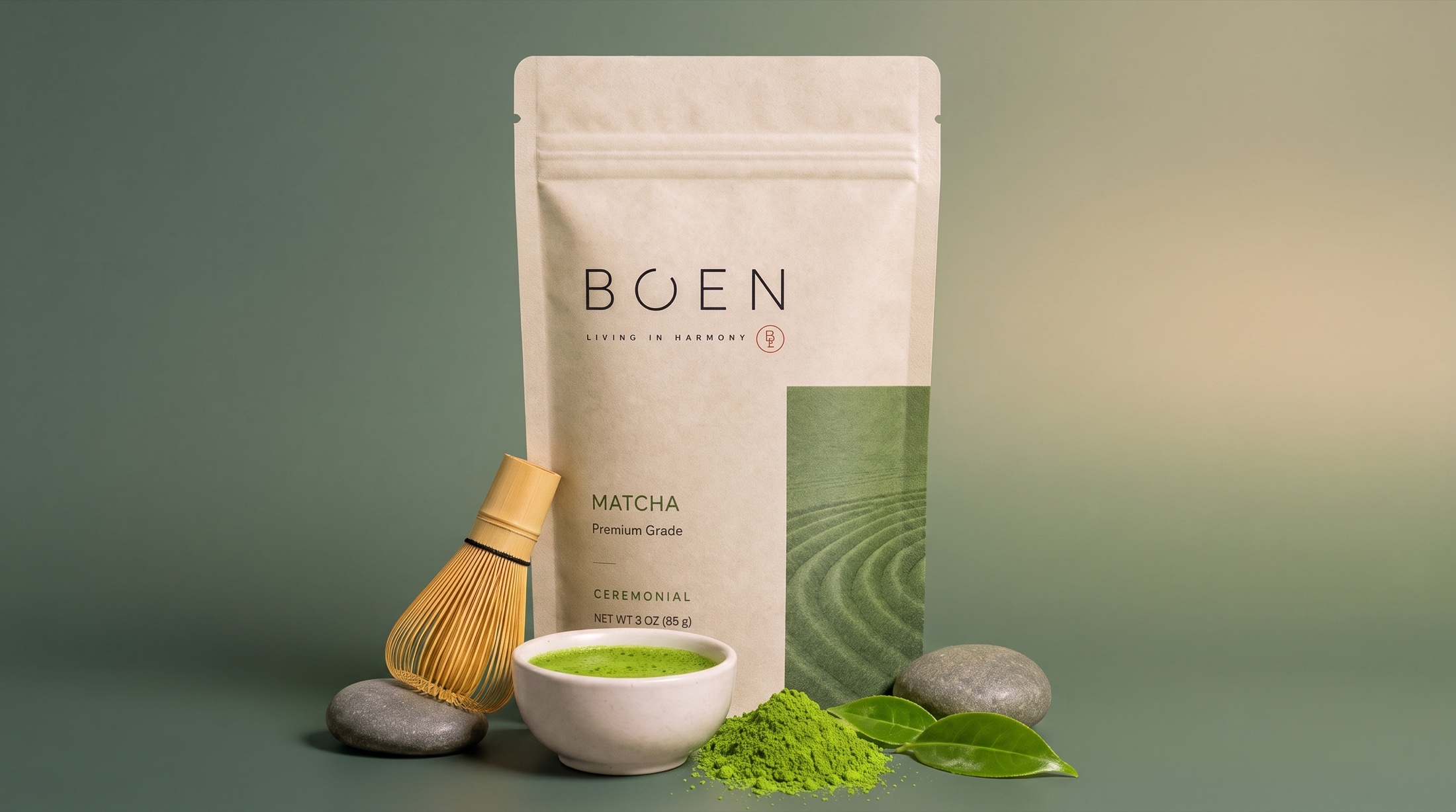 BO'EN ceremoniell matcha i greige påse på en natursten, omgiven av nyvispad matcha i en skål, en bambuvisp och färska teblad